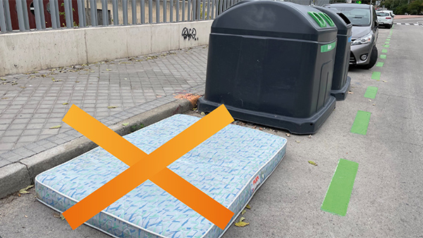 colchón abandonado en la calle junto a un contenedor de vidrio